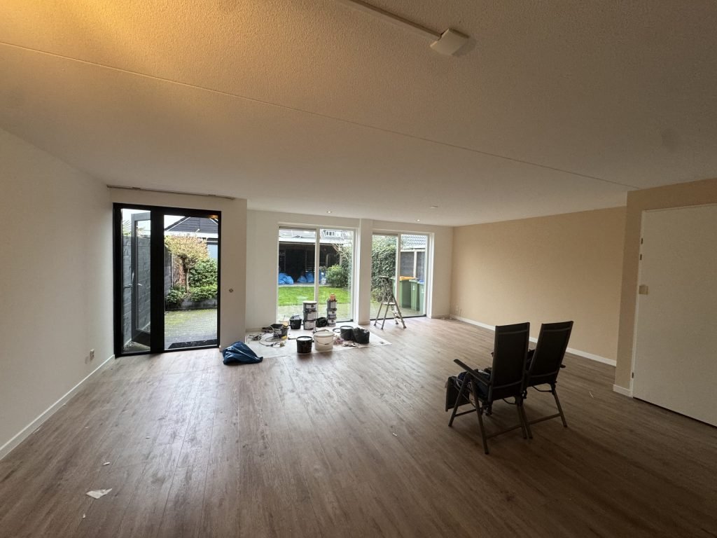 Ruime woonkamer met lichte wanden, een houten vloer en openslaande tuindeuren, midden in de afwerking
